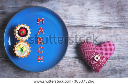 Postcard Greetings from the International Women's Day March 8, on a light wooden background blue ceramic plate with two cakes