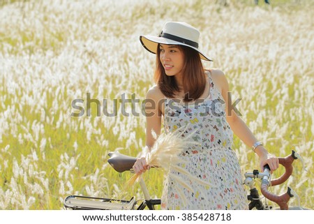A girl with vintage bicycle at meadow in the early morning. Sun shine with golden light, silhouette back light on her body and grass flowers. Image create for people, healthcare, fashion and cosmetic.