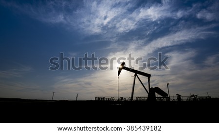 Silhouette of crude oil pump at cloudy sunset in oil field.