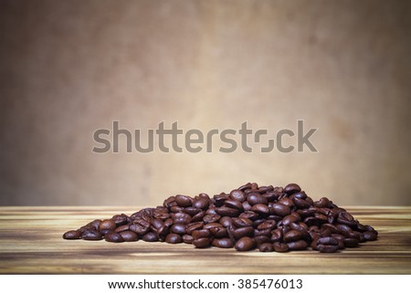 Pile of coffee beans on wooden table opposite a defocused burlap background. Shallow depth of field. Toned.