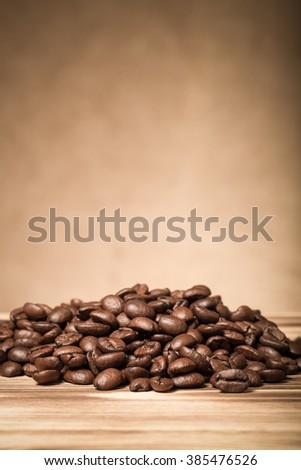 Pile of coffee beans on wooden table opposite a defocused burlap background. Shallow depth of field. Toned.