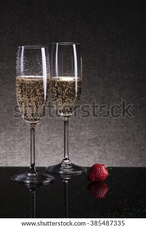 Two glasses of champagne with strawberries on a black table, shot in low key