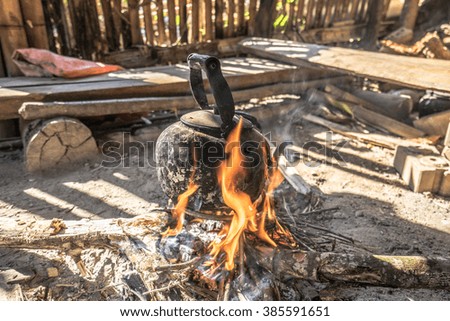 Old style/Traditional fireplace/kitchen with bunch of burning firewood to boil water in the old aluminum kettle with the scene of the shade of the housing of the hill tribes.