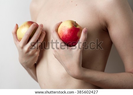 One Caucasian girl covers her Breasts with two red apples on a light background