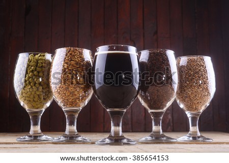 Glasses filled with dark beer, different malts and hops over a wooden background Royalty-Free Stock Photo #385654153