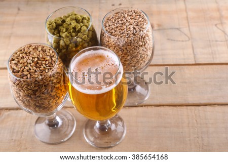 Glasses full of light beer, different types of malt and hops over a wooden background Royalty-Free Stock Photo #385654168