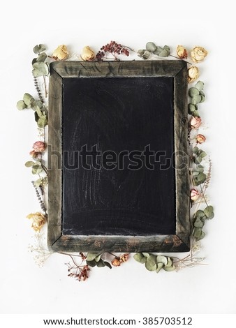 Clean black wooden chalkboard with yellow and pink roses and green leaves. Flat lay