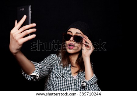 Hipster cool girl taking picture on smartphone self-portrait,  snapshot studio on a black background