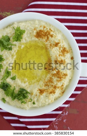 Fresh bowl of homemade hummus with chickpeas, olive oil, cayenne pepper and parsley. Red background
