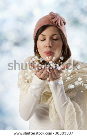 pretty sweet girl blowing on snow flakes with white scarf and a pink winter cap in a studio shot