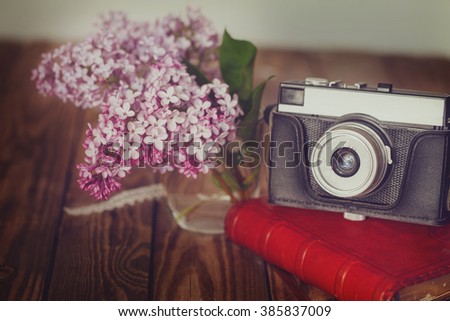 Vintage camera and Bouquet of lilac spring flowers on wooden background.Toned image