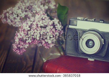 Vintage camera and Bouquet of lilac spring flowers on wooden background.Toned image
