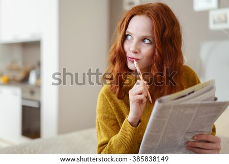 Thoughtful young woman doing a cryptic crossword puzzle in a newspaper looking off to the side with a pensive expression as she tries to solve a clue Royalty-Free Stock Photo #385838149