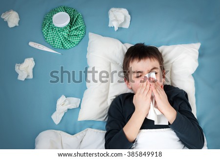 Ill boy lying in bed. sad child with fever and ice bag on head  Royalty-Free Stock Photo #385849918