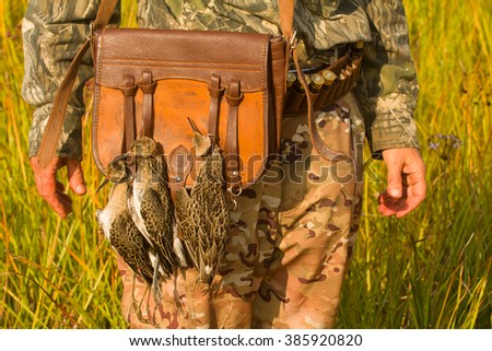 Gourmet game 3. Hunting  fowling bag leather and waders as trophy on game strap. Photo was taken in swamp, in hunting area. Hunting camouflage clothing