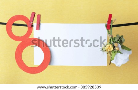 figure 8, paper flowers hang on clothespins in front of yellow background. International Women's Day. March 8, Happy Women's Day greeting message text