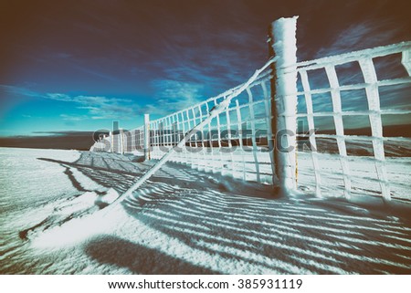 A frozen wire fence below the summit of Geal-charn Mor, Cairngorms in the Scottish Highlands, UK. Added grain and colour styling.