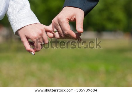 Lovers or bride and groom hold little fingers or pinky. hand with ring. Hands of men and women in the upper left corner of the picture. The green lawn in the background.