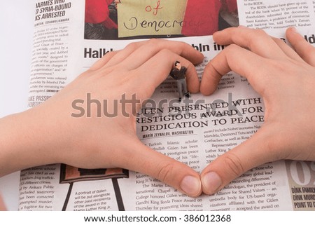 Human figure in the middle of a hand making a heart shape on a newspaper