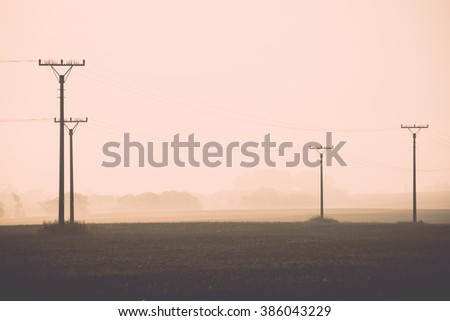 sunset over the fields in fog in summer with electricity poles - vintage effect
