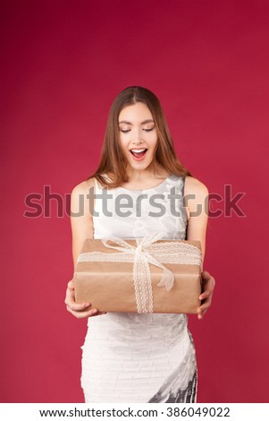 a beautiful young girl with a box wrapped in gift paper in hands on red background
