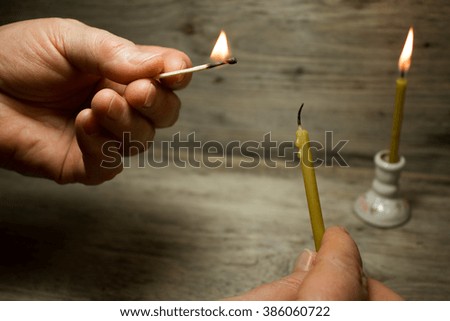 A lighted match in his hand and the candle, Matches with blue heads on wooden background