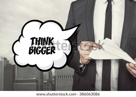 Think bigger text on speech bubble with businessman holding paper plane in hand