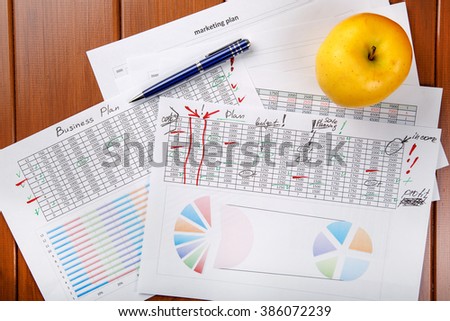 Business records, budget planning and marketing plans, documents for work and an yellow apple for a snack.