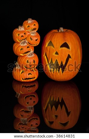 Halloween Jack O Lanterns already carved and sitting on a table.  One large pumpkin and one stack of 6 small pumpkins on black background with reflection.