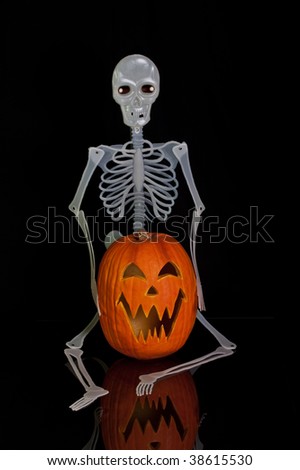 A Skeleton holding a Halloween Jack O Lantern and sitting on a table with reflection.
