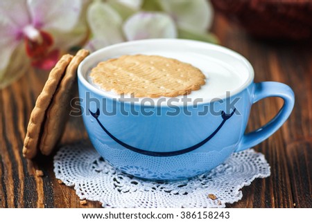 Good morning or Have a nice day message concept - bright blue cup of milk with cookies. Cup of milk with smile. Health and diet concept on the wooden table, close up.