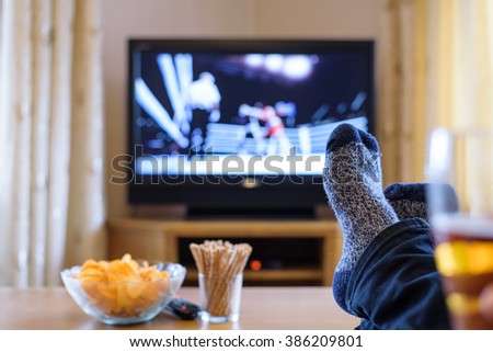 Television, TV watching (boxing match) with feet on table eating snacks and drinking beer - stock photo