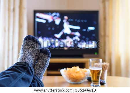 Television, TV watching (basketball game) with feet on table eating snacks and drinking beer - stock photo