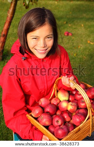 Apple picking in the fall - beautiful young woman with basket full of red apples.