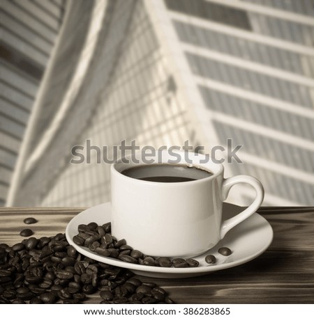 Coffee beans and coffee in white cup on wooden table opposite a defocused cityscape for background. Collage. Selective focus. Toned.