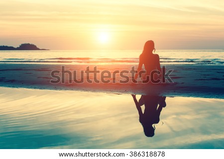 Young woman sitting on the beach, silhouette at sunset.