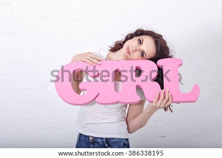 Young cute girl holding a pink lettering girl. Human emotions. Girl in a white T-shirt.