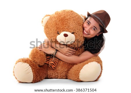 Beautiful Asian girl wearing fedora hat, hugging her big brown teddy bear from behind and smiling to camera, isolated on white background