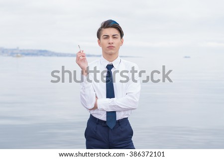 stylish teen in a shirt and tie smokes on the background of the sea