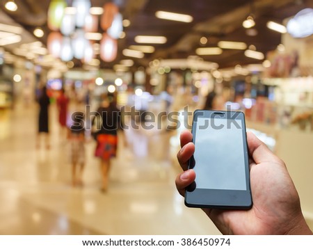 Hand hold and touch screen smart phone on shopping mall blurred background concept.