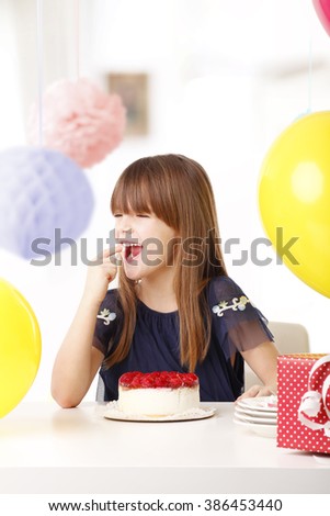 Close-up portrait of adorable little girl tasting her birthday cake at party.