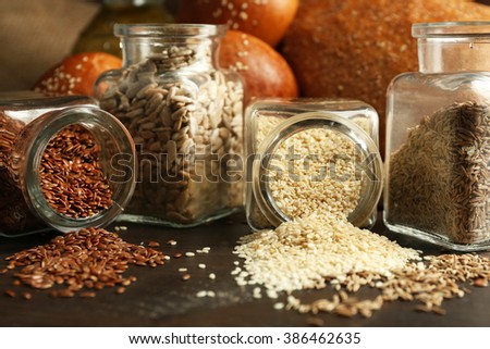 Composition of seeds in banks, bread, buns and oil on wooden table background, closeup