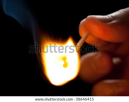 Hand holding a burning match on black