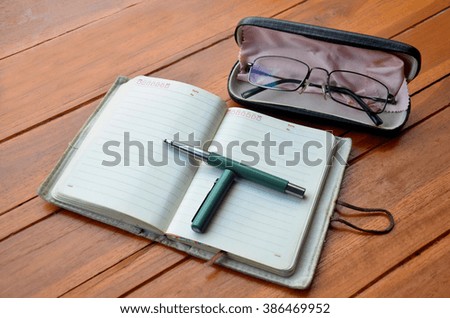 Pen on note book and Spectacles glasses on wooden table