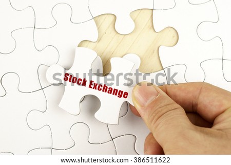 Finance concept. Hand holding piece of jigsaw puzzle showing STOCK EXCHANGE word.