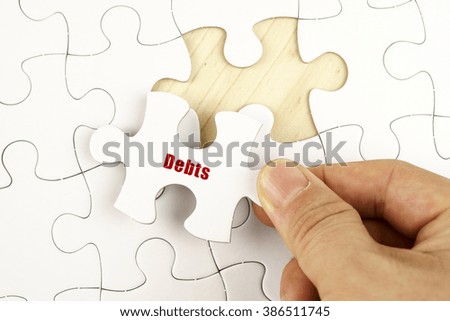 Finance concept. Hand holding piece of jigsaw puzzle showing DEBTS word.