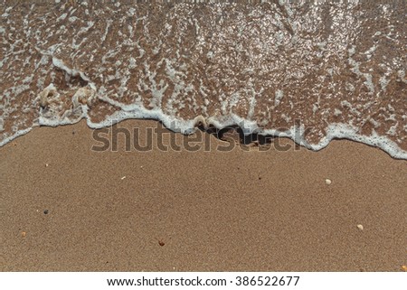 Wave washes away the footprints in the sand. Abstract background