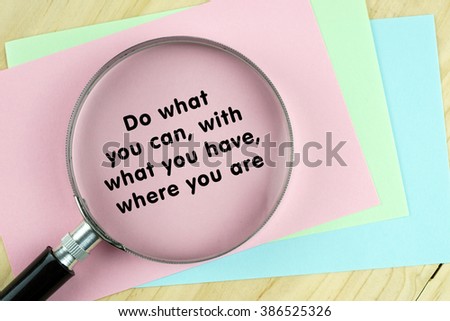 Magnifying glass on papers with word quote of "Do what you can,with what you have,where you are" written on it.