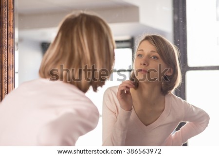 Young Woman Looking in Mirror Royalty-Free Stock Photo #386563972