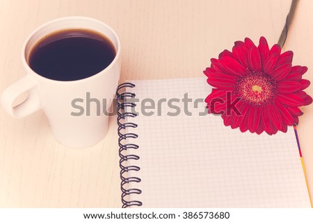 Red gerbera flower,cup of coffee and notebook on the wooden desk. Selective focus, toned